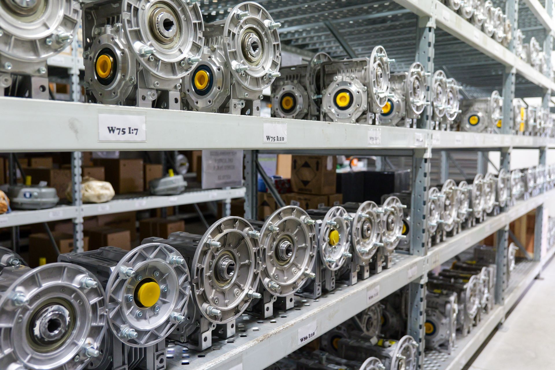 In un magazzino, scaffali industriali pieni di numerosi riduttori circolari argentati con tappi centrali gialli.