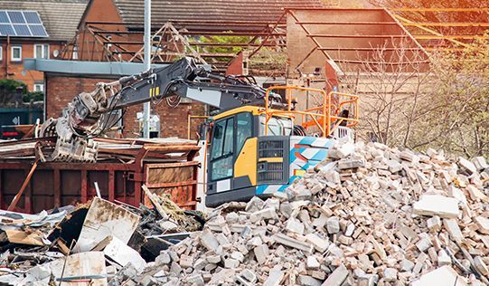 a bulldozer is demolishing a building with a pile of bricks in the foreground .