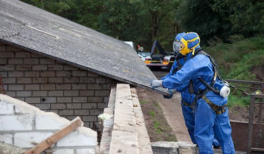 a man in a protective suit is cutting a piece of asbestos from a roof .