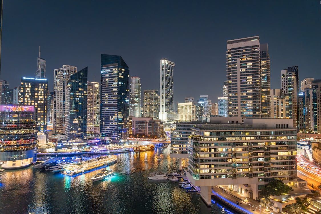 Wooden boat in turquoise water, harbor with white yachts and buildings in background.