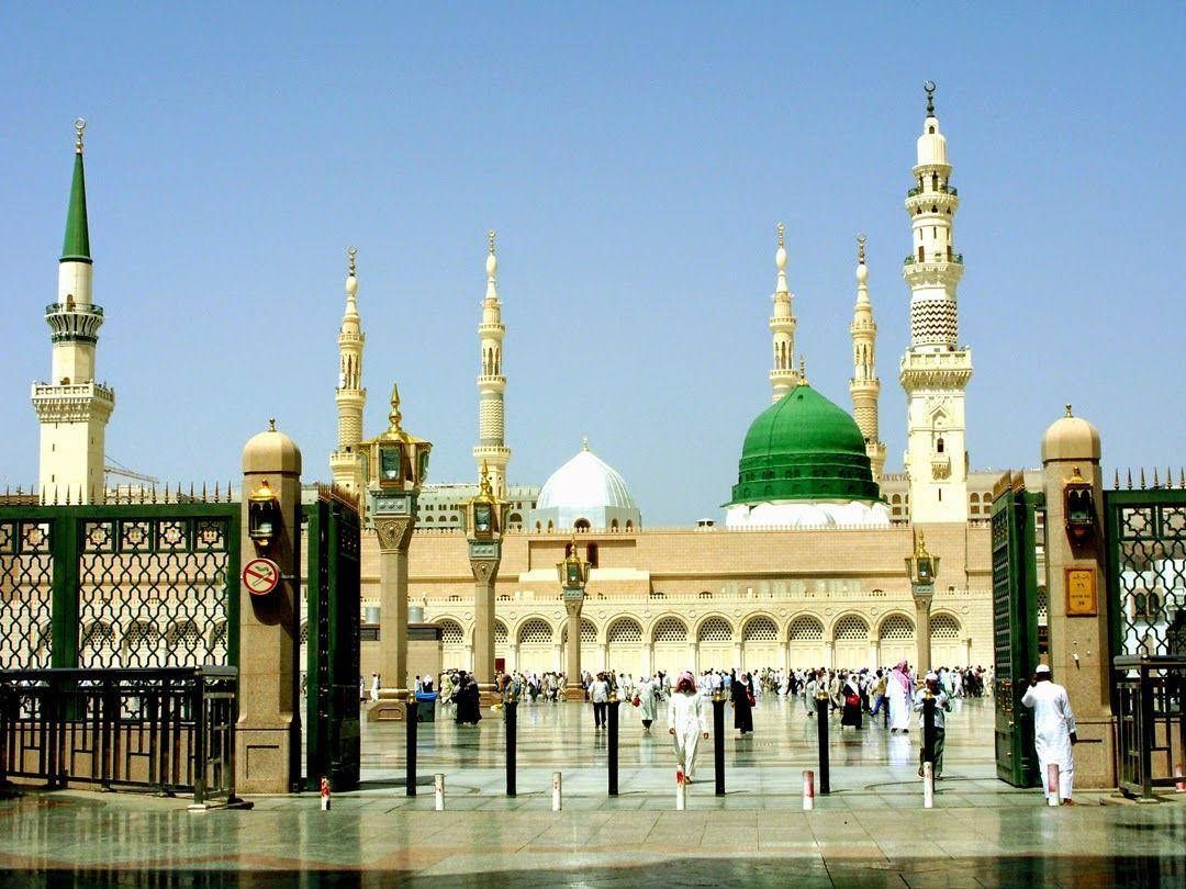 The Prophet's Mosque in Medina, Saudi Arabia, with green dome and minarets, people walking.