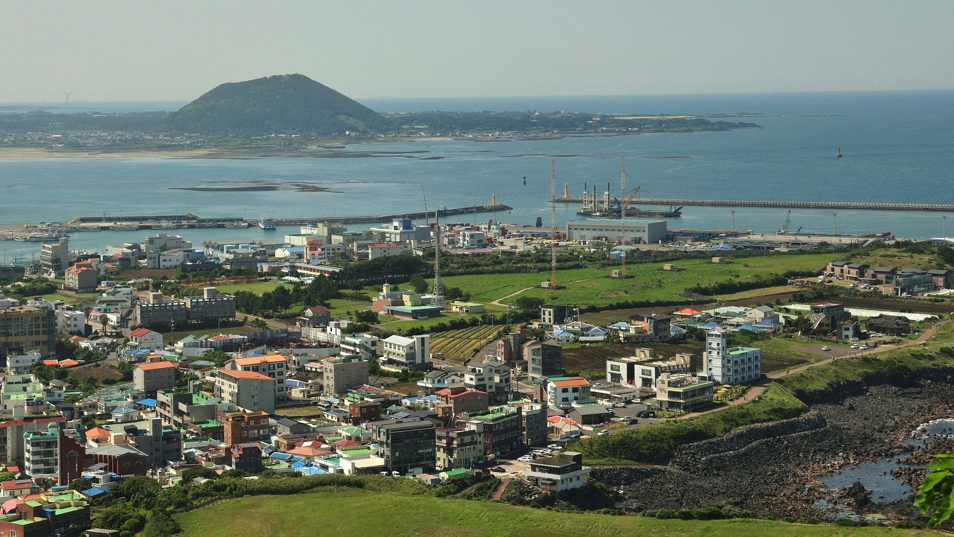 Wooden boat in turquoise water, harbor with white yachts and buildings in background.
