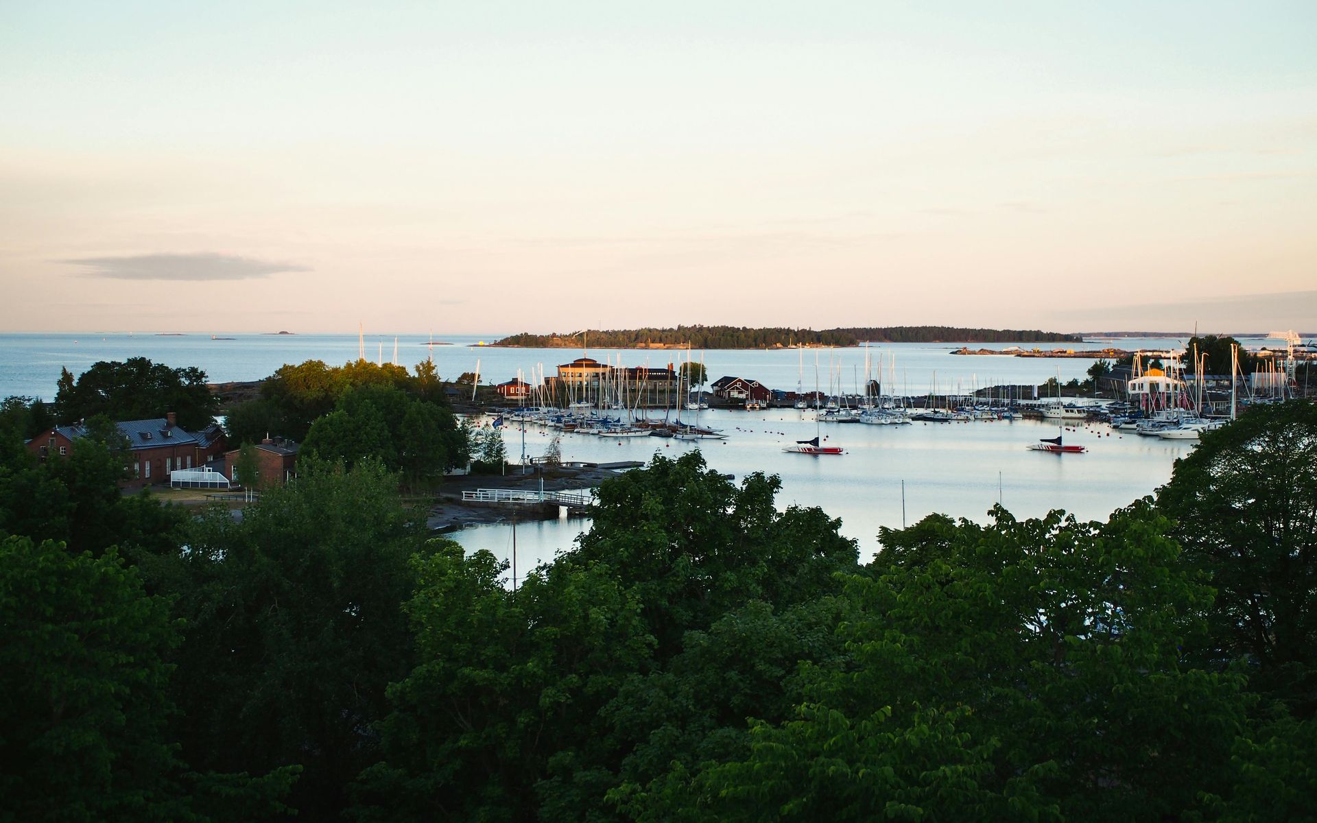 Wooden boat in turquoise water, harbor with white yachts and buildings in background.