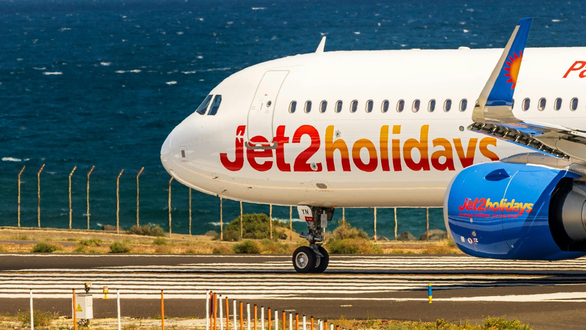 Jet2Holidays plane on a runway, ready for takeoff at an airport. Advertisement for booking holidays.