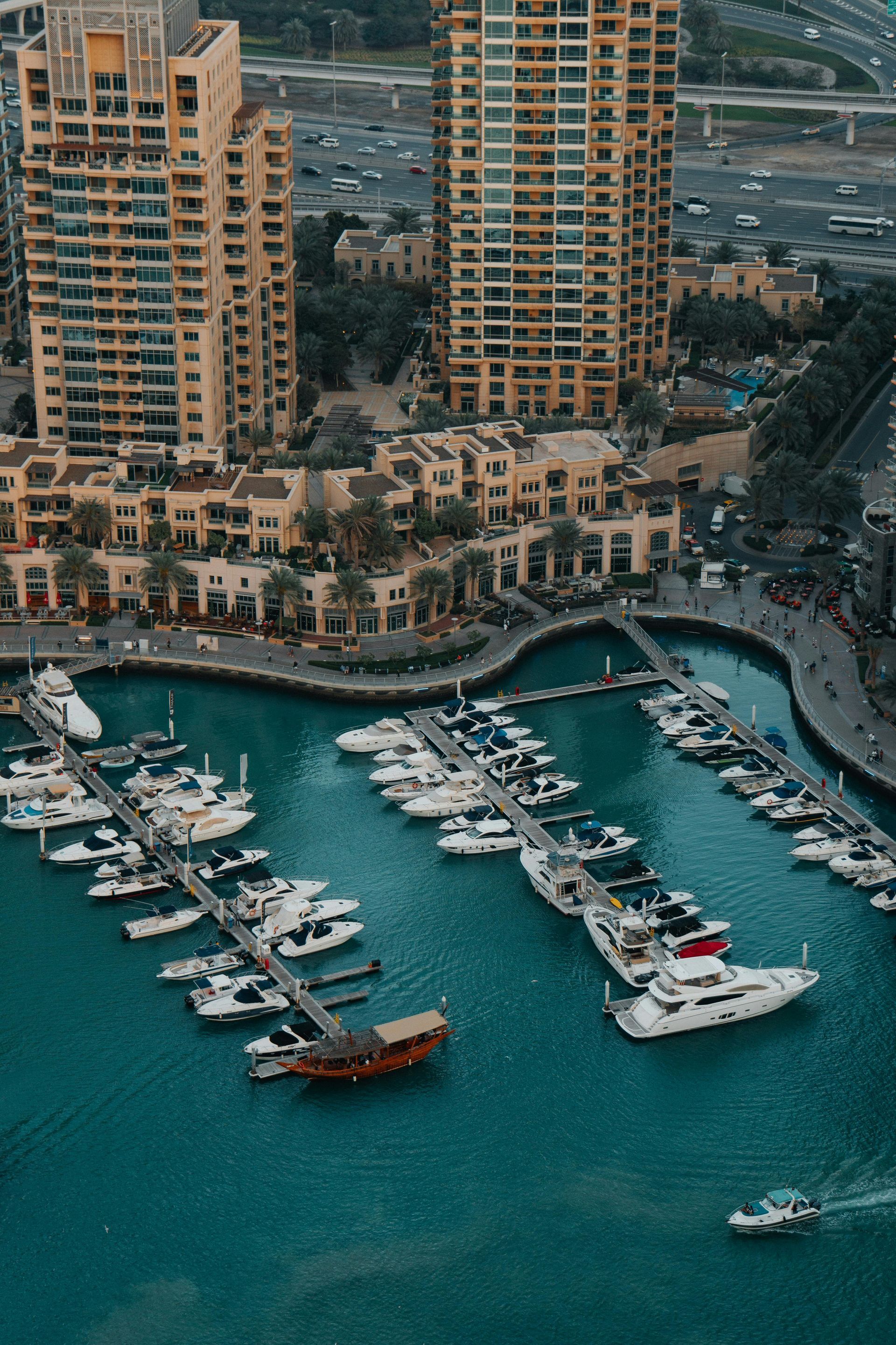 Wooden boat in turquoise water, harbor with white yachts and buildings in background.