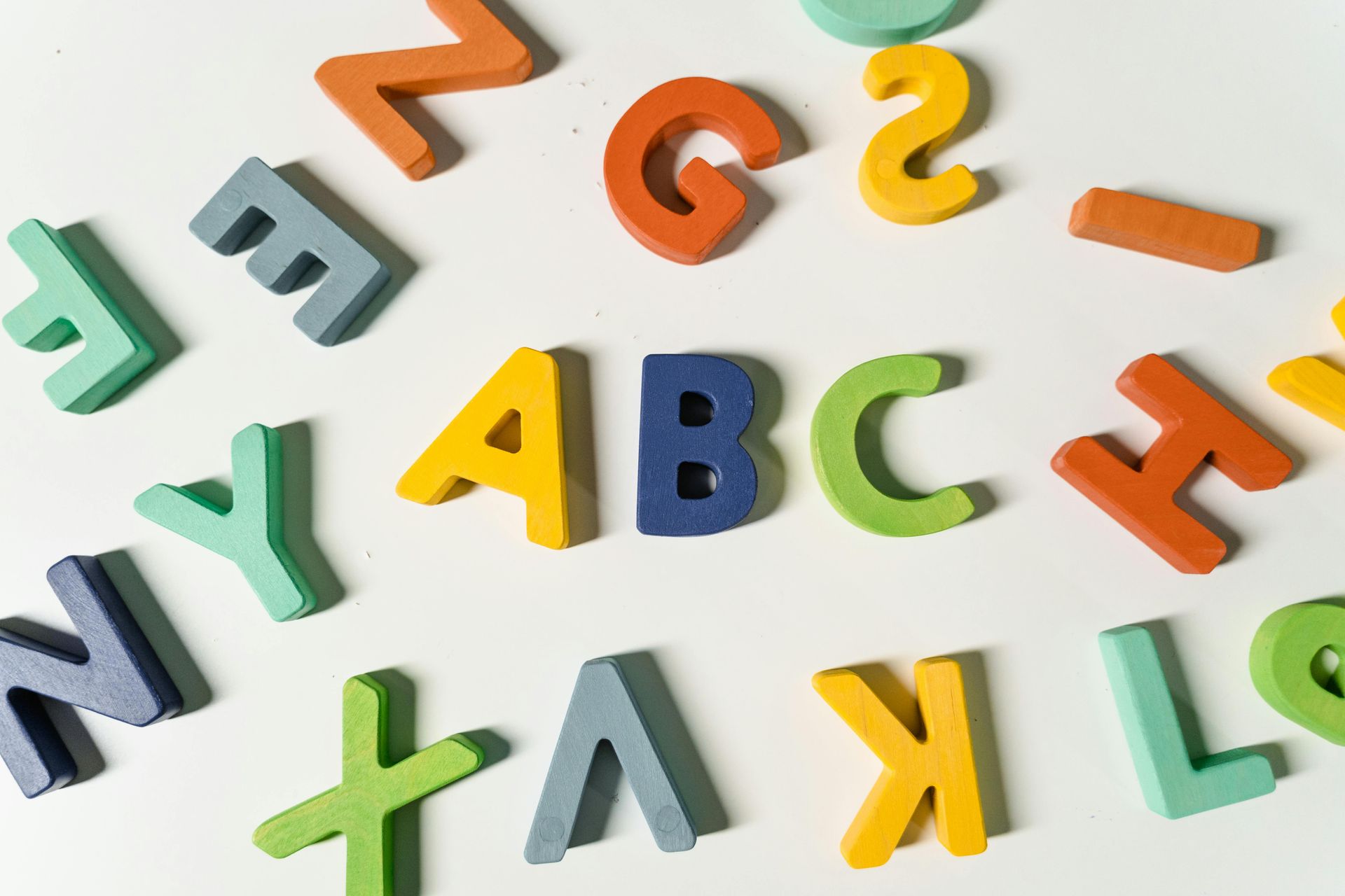 Colorful wooden alphabet letters scattered on a white surface, spelling ABC in the center.