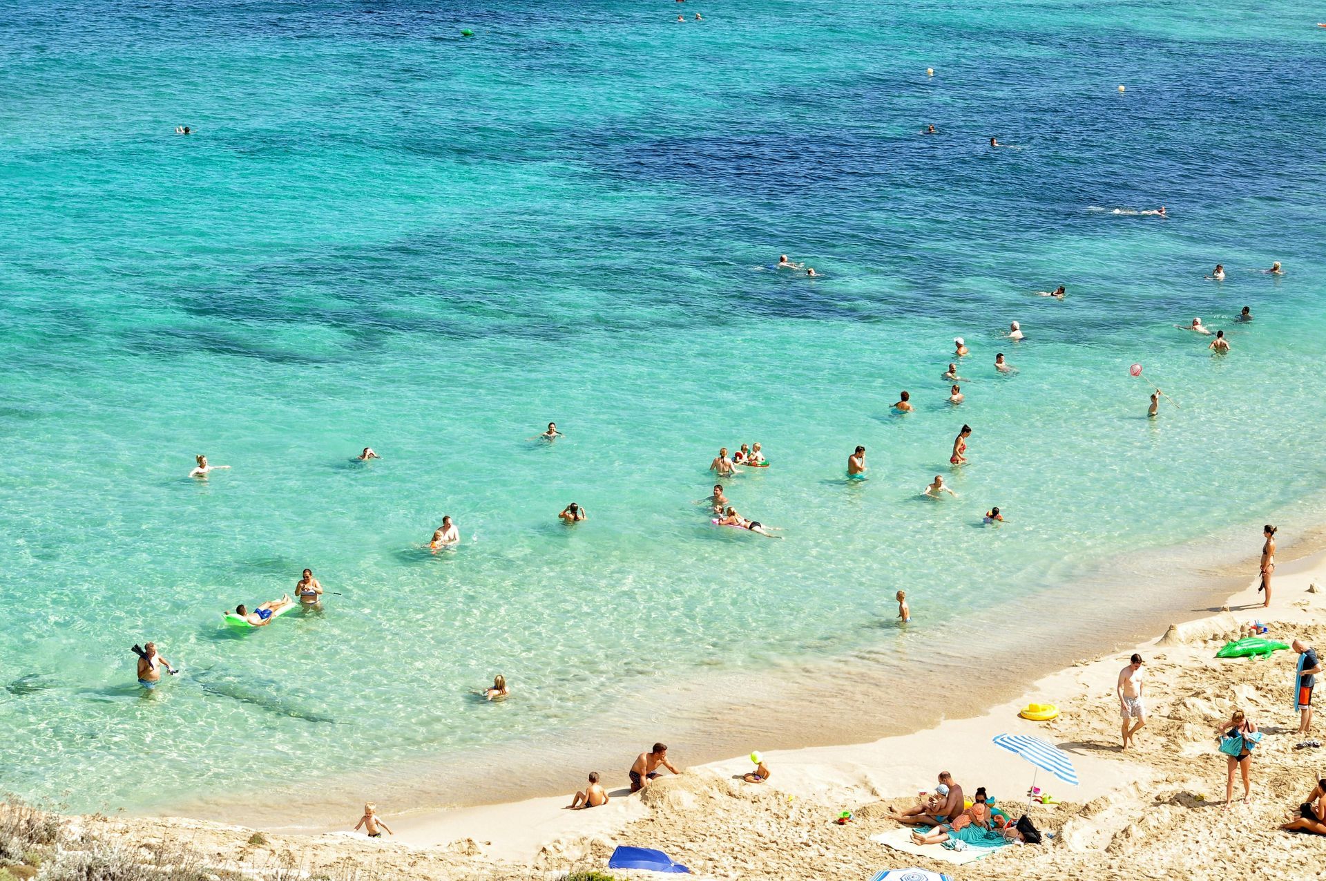 Beach with turquoise water, swimmers, and people on the sandy shore on a sunny day.