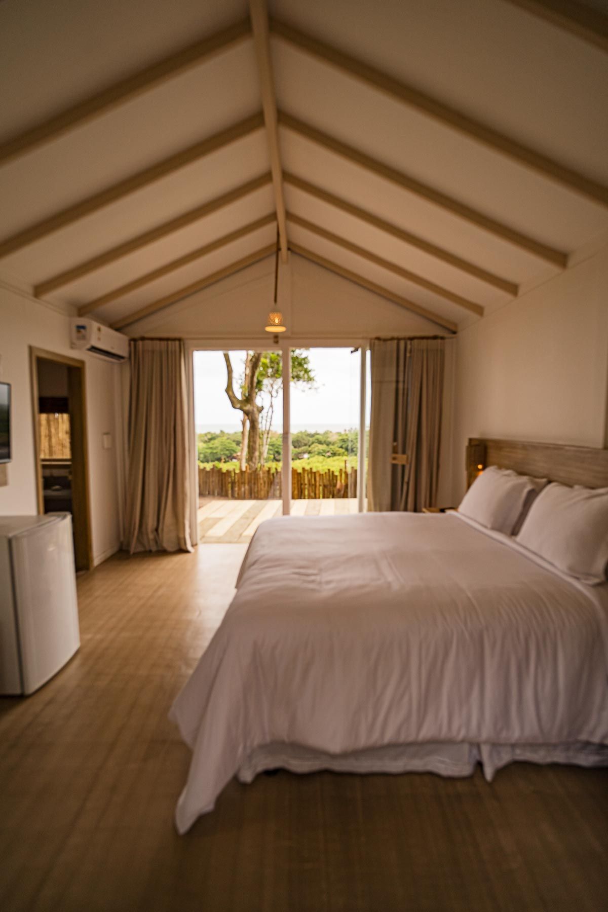 Piscina com espreguiçadeiras, mesas e guarda-sóis em um deck de madeira com vista para uma paisagem verdejante sob um céu azul.