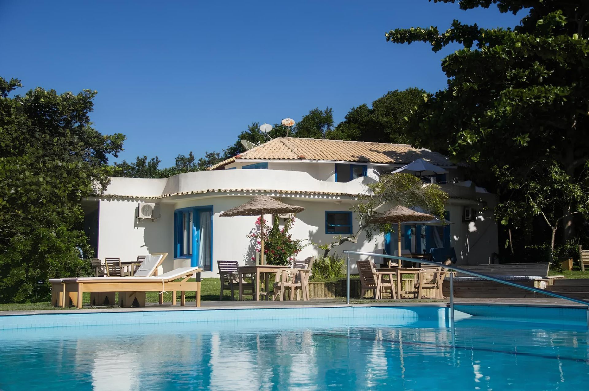 Resort à beira da piscina com um prédio branco, portas azuis e guarda-sóis.
