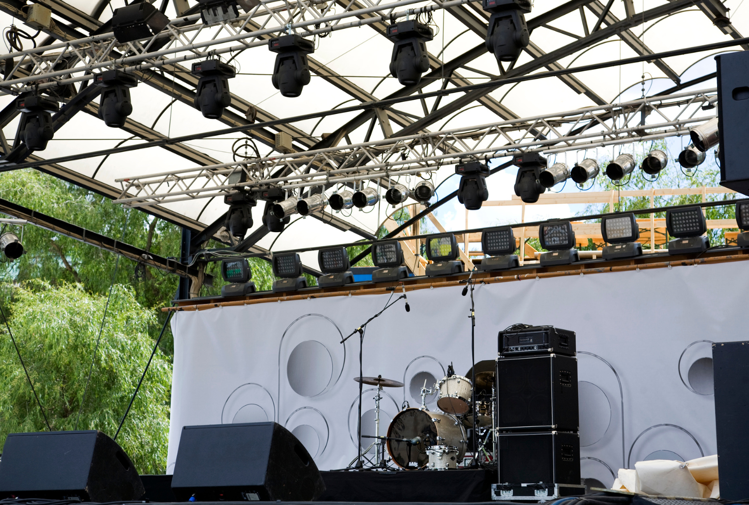 An empty stage with a drum set and speakers under a canopy.