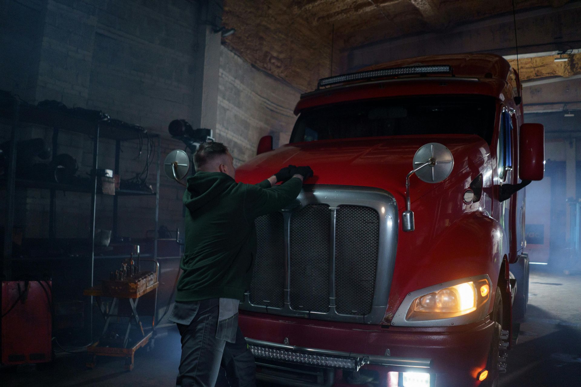 Man changing a flat tire; pointing at the wheel; tools in a box on the ground; black car; asphalt.