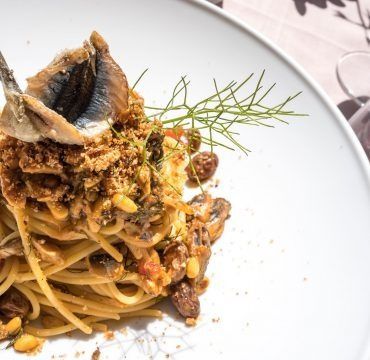 Un piatto bianco con sopra degli spaghetti e un pesce su un tavolo.