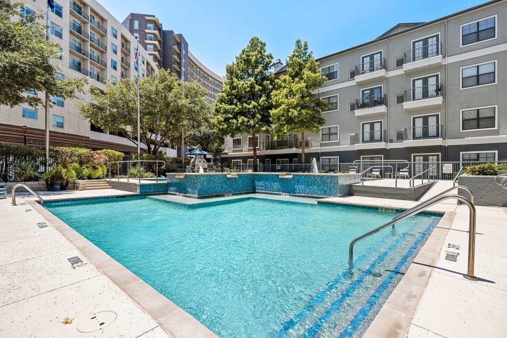 Resort-style swimming pool in front of the apartment building with stairs leading to it at Marquis at Texas Street in Dallas, TX.