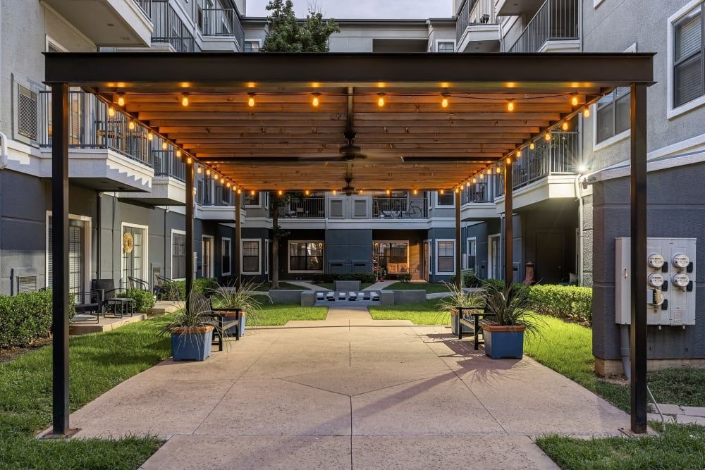 A pergola with lights on it in front of the apartment building at Marquis at Texas Street in Dallas, TX.