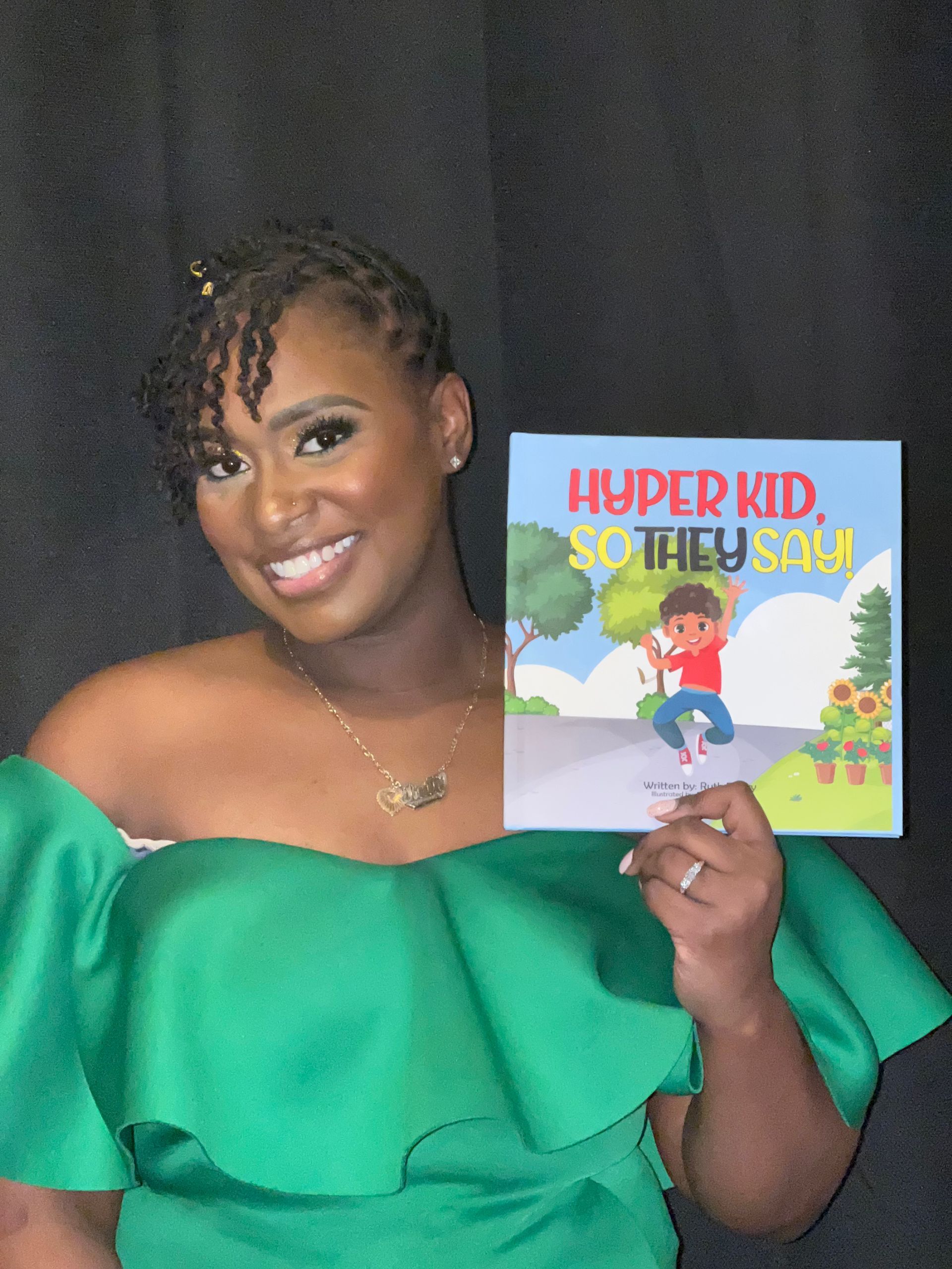 Woman in green dress smiles, holding book 