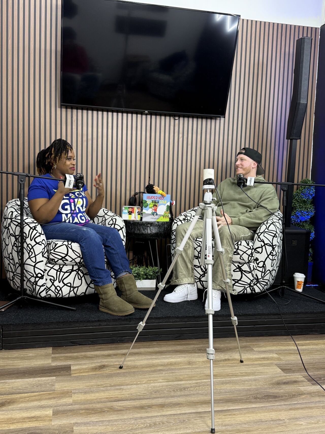 Two people in beanbag chairs, talking during a podcast. Microphone on tripod in foreground.