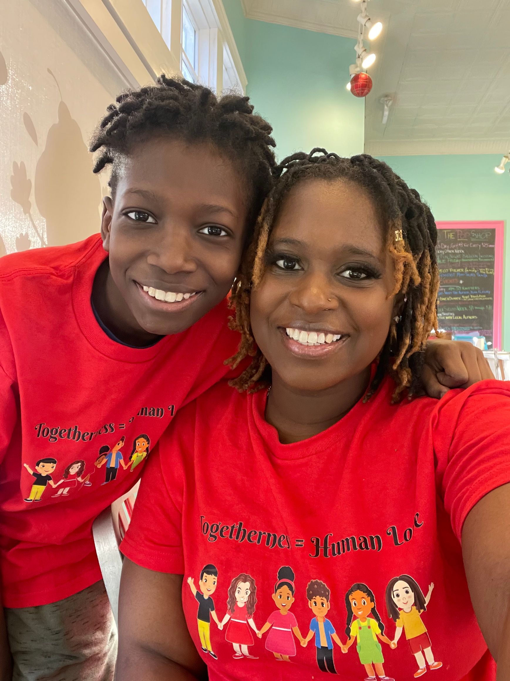 Two people smiling, wearing red shirts with a colorful cartoon. Indoors with light-colored walls.