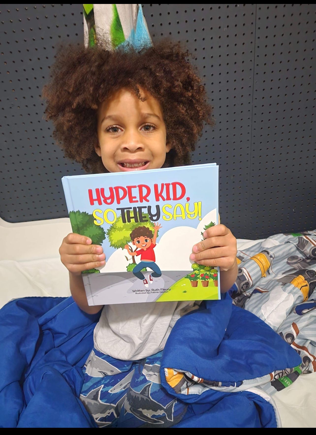 Young child smiling, holding a book titled 