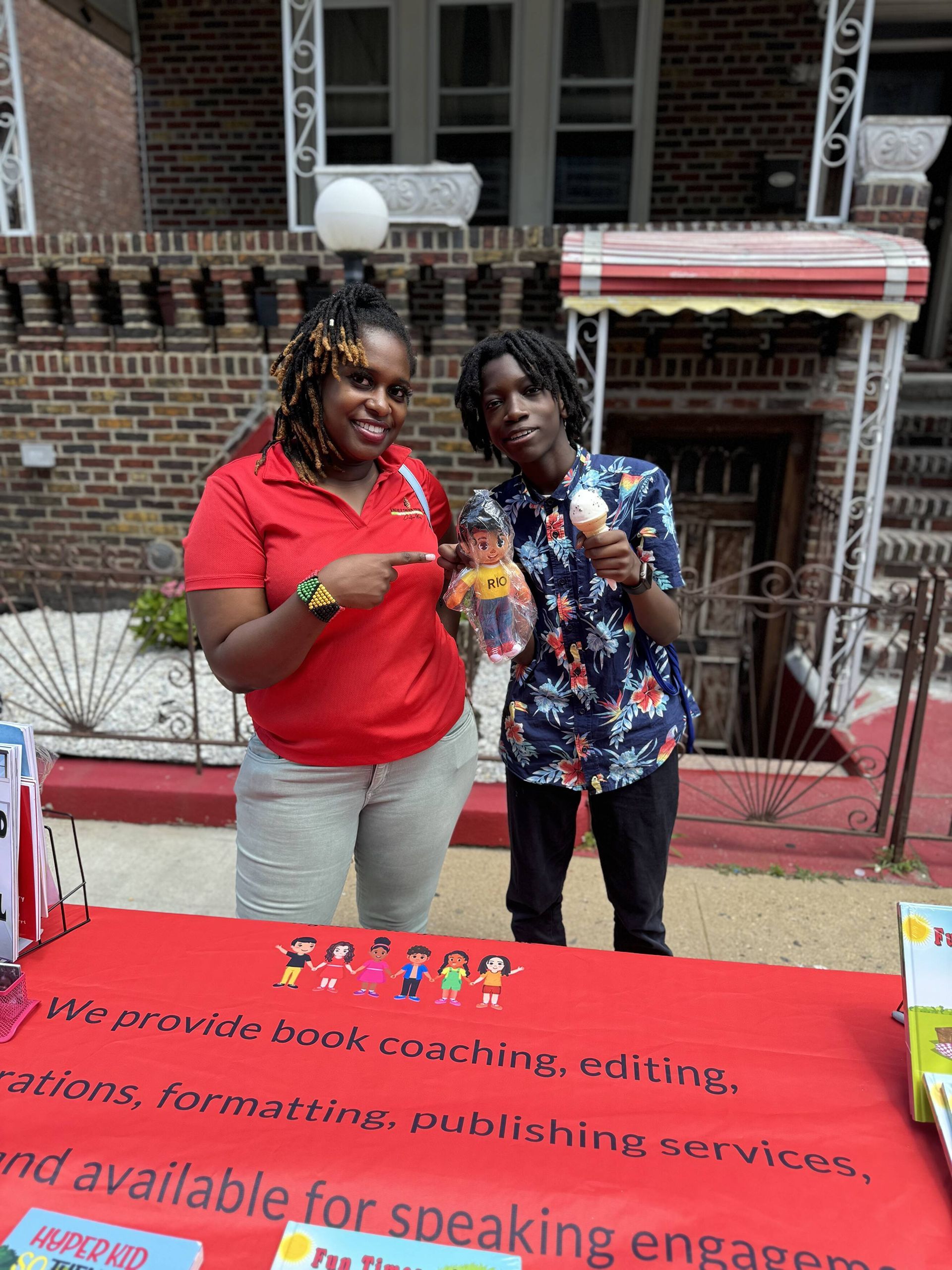 Two people standing behind a table with books. One points, the other holds an ice cream cone.