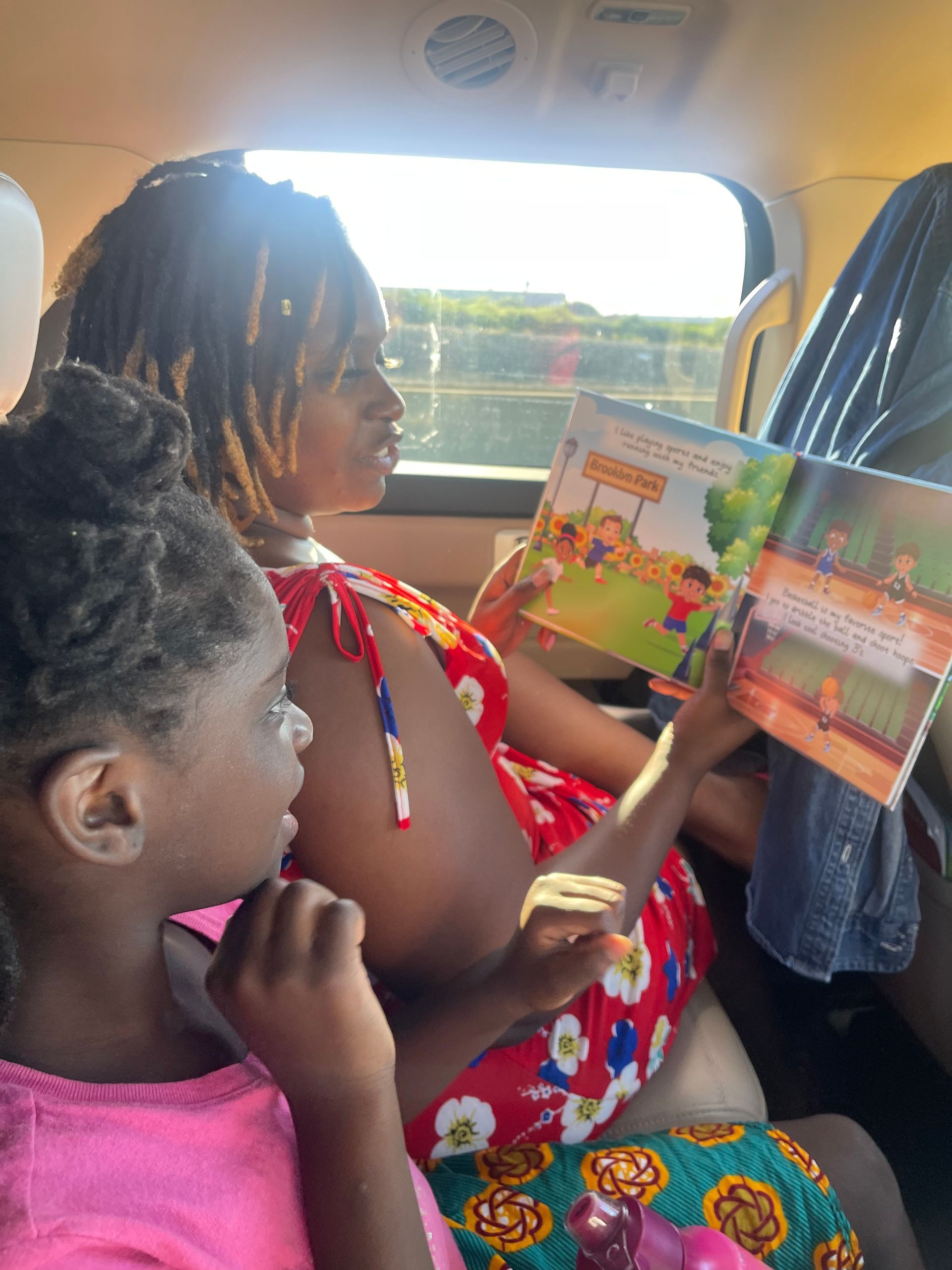 Woman reads to child in a car; book shows illustrations. They are near a window, lit by sunlight.