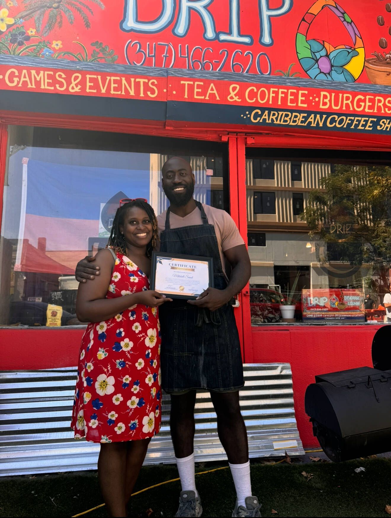 Two people pose in front of a red food truck, holding a certificate.