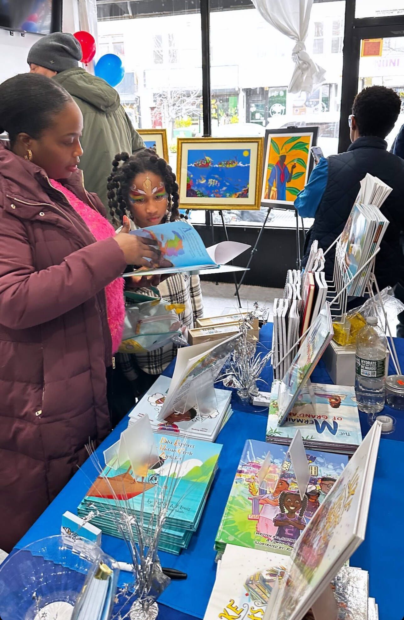 Woman and child looking at books at an event, with artwork and other attendees in the background.