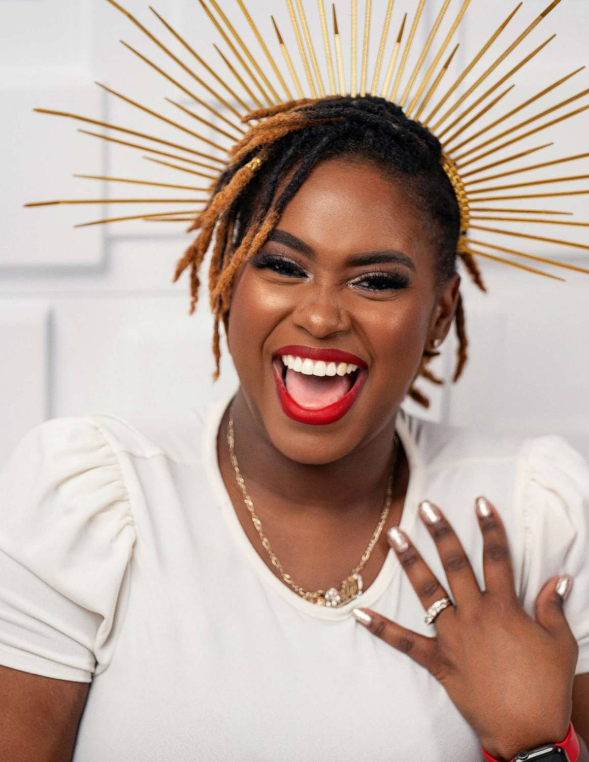 A woman wearing a white shirt and a gold headpiece is smiling.