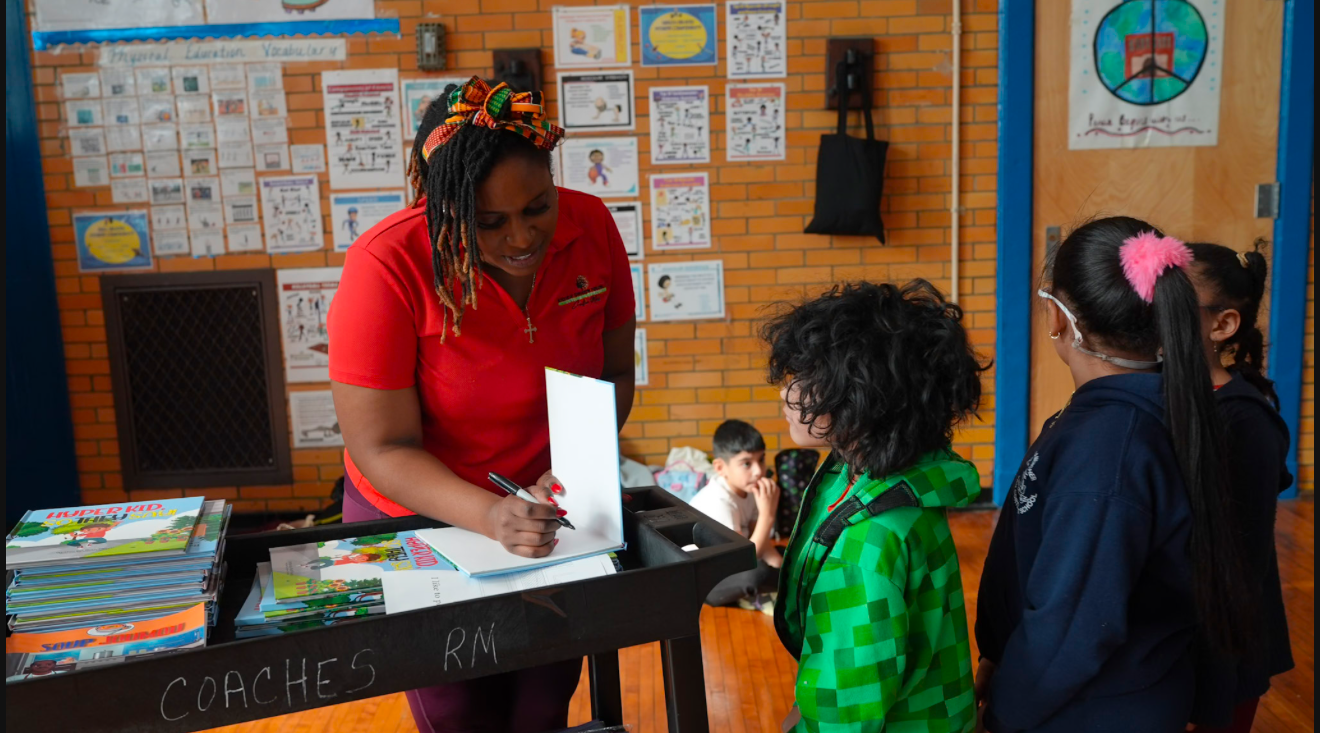Woman signing books at a table, interacting with a group of children in a classroom.