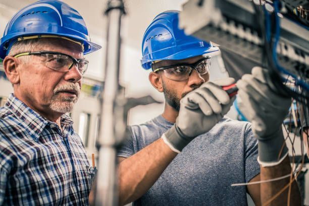 Two men wearing hard hats and safety glasses are working on a machine.