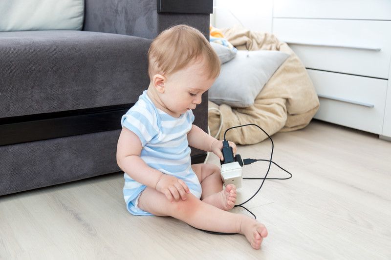 A baby is sitting on the floor playing with a plug.