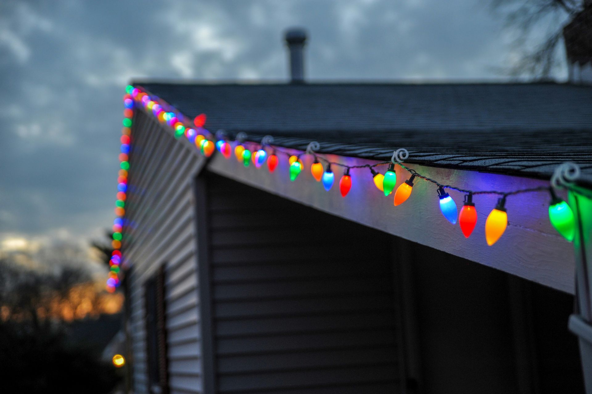 A string of colorful Christmas lights hanging from the roof of a house.