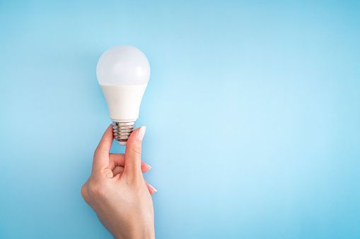 A woman is holding a light bulb in her hand on a blue background.