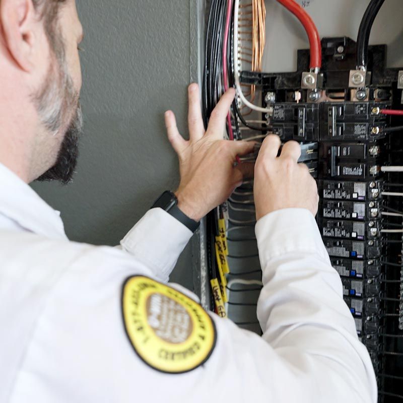 A Mr Sparky Electrician in a white shirt inspects a circuit breaker panel