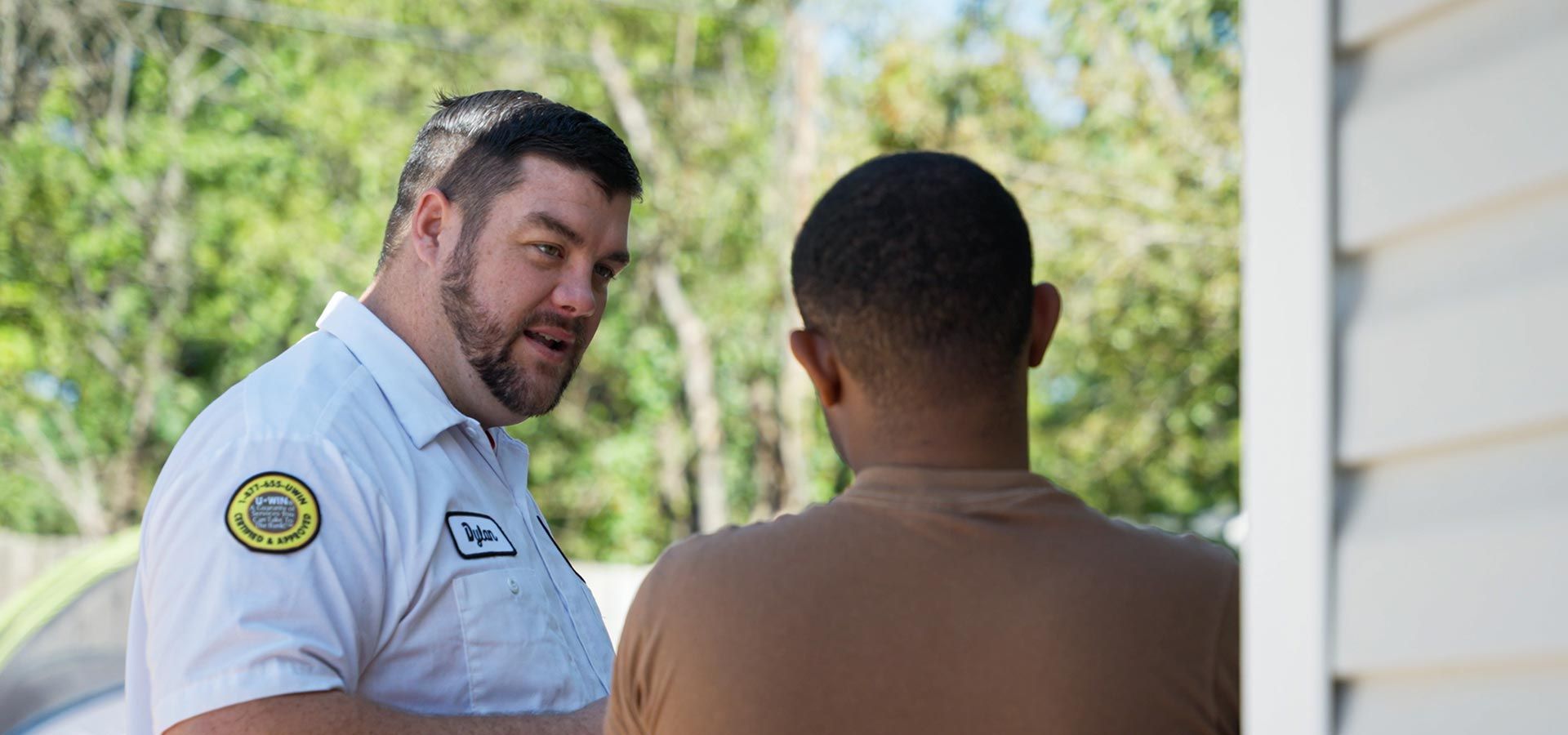 a man in a white shirt is talking to another man in a brown shirt.