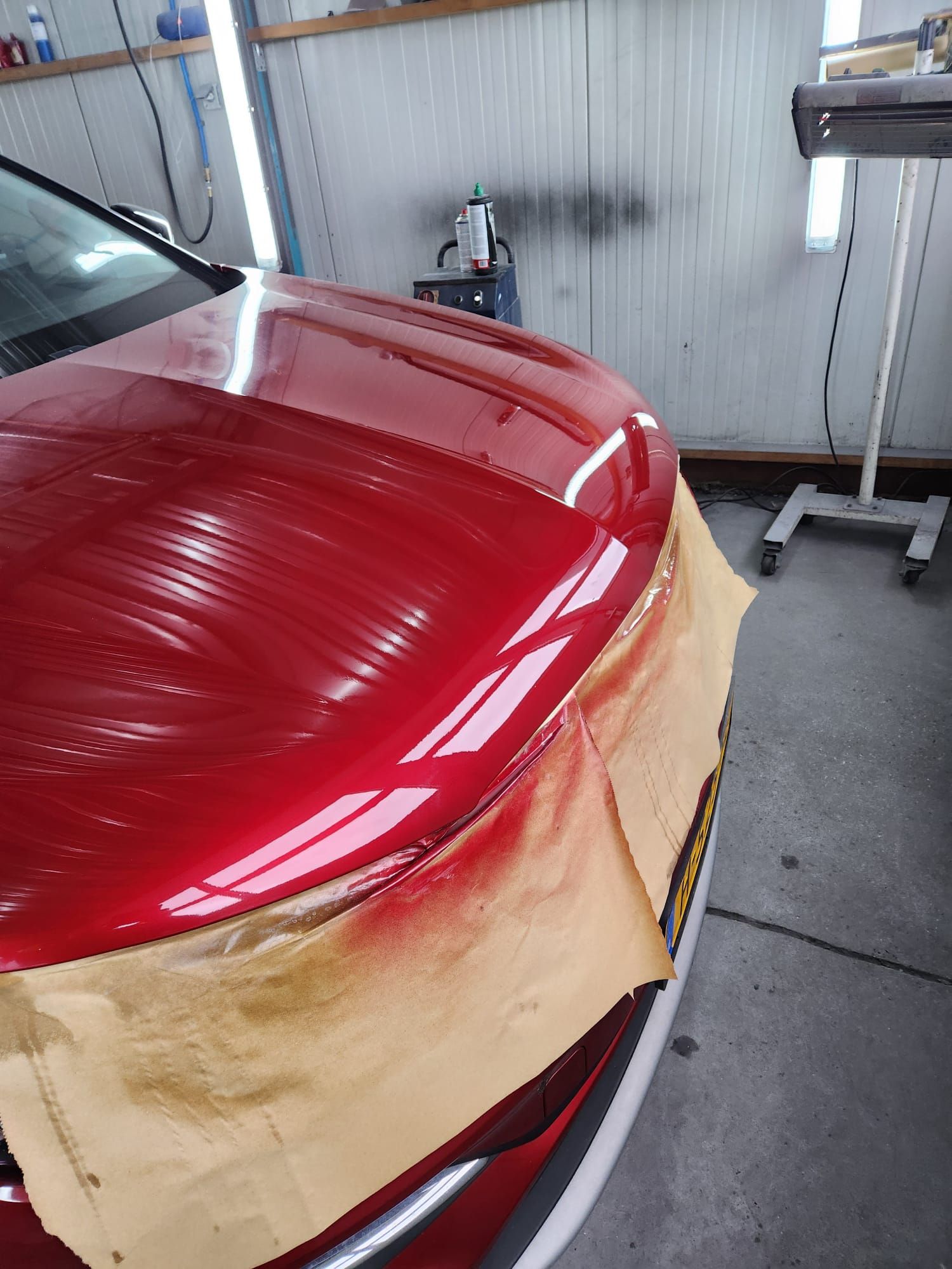Een rode auto wordt geschilderd in een garage door spotrepair van werner uit loenen. 