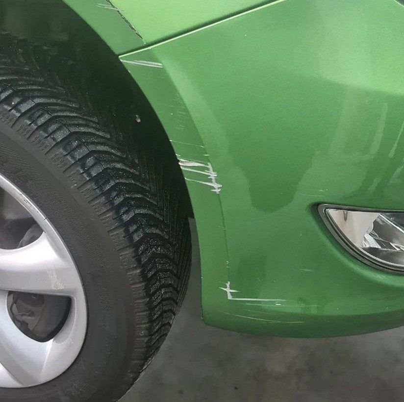 Een groene auto heeft een kras op de voorbumper