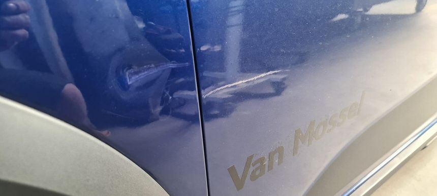 Een close-up van een blauwe auto met een deuk op de zijkant.