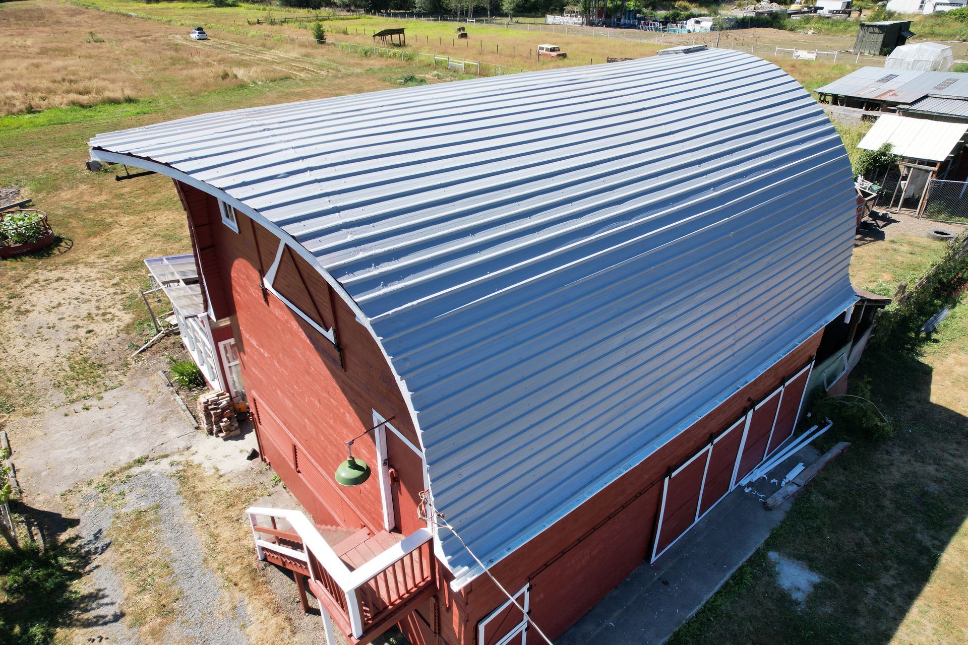 An aerial view of a red barn with a white roof taken by Riverside Roofing