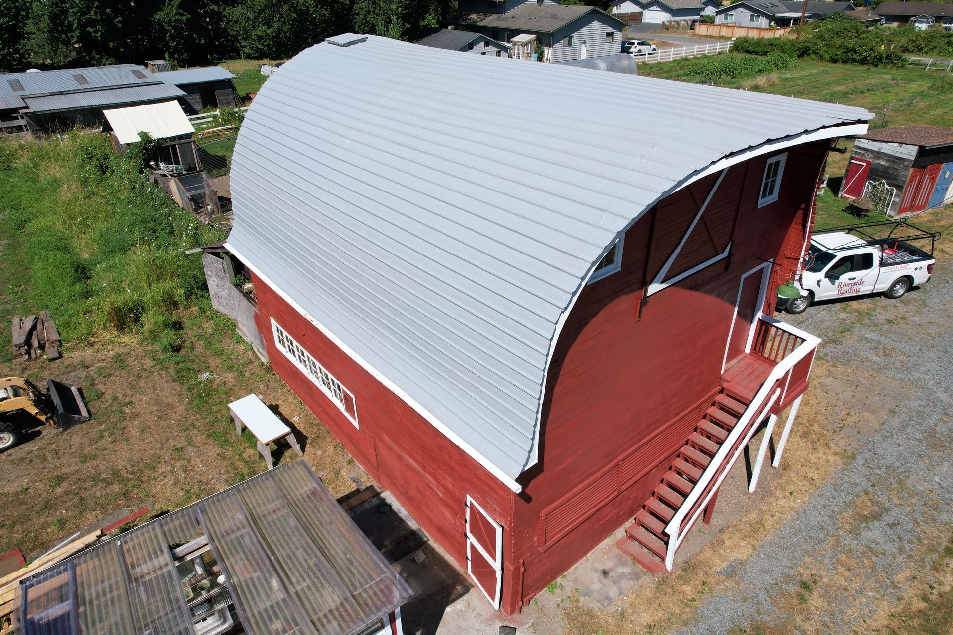 An aerial view of a red barn with a new curved roof taken by Riverside Roofing