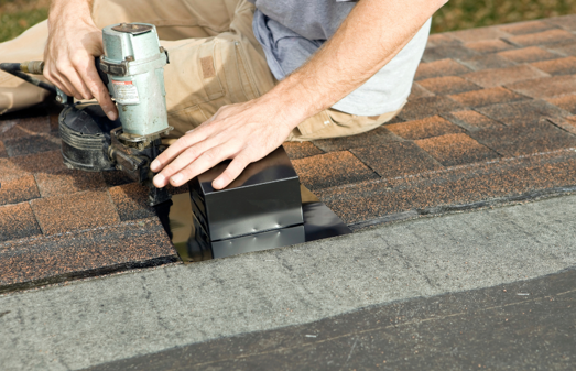 A man installs an attic ventilation system onto a roof.