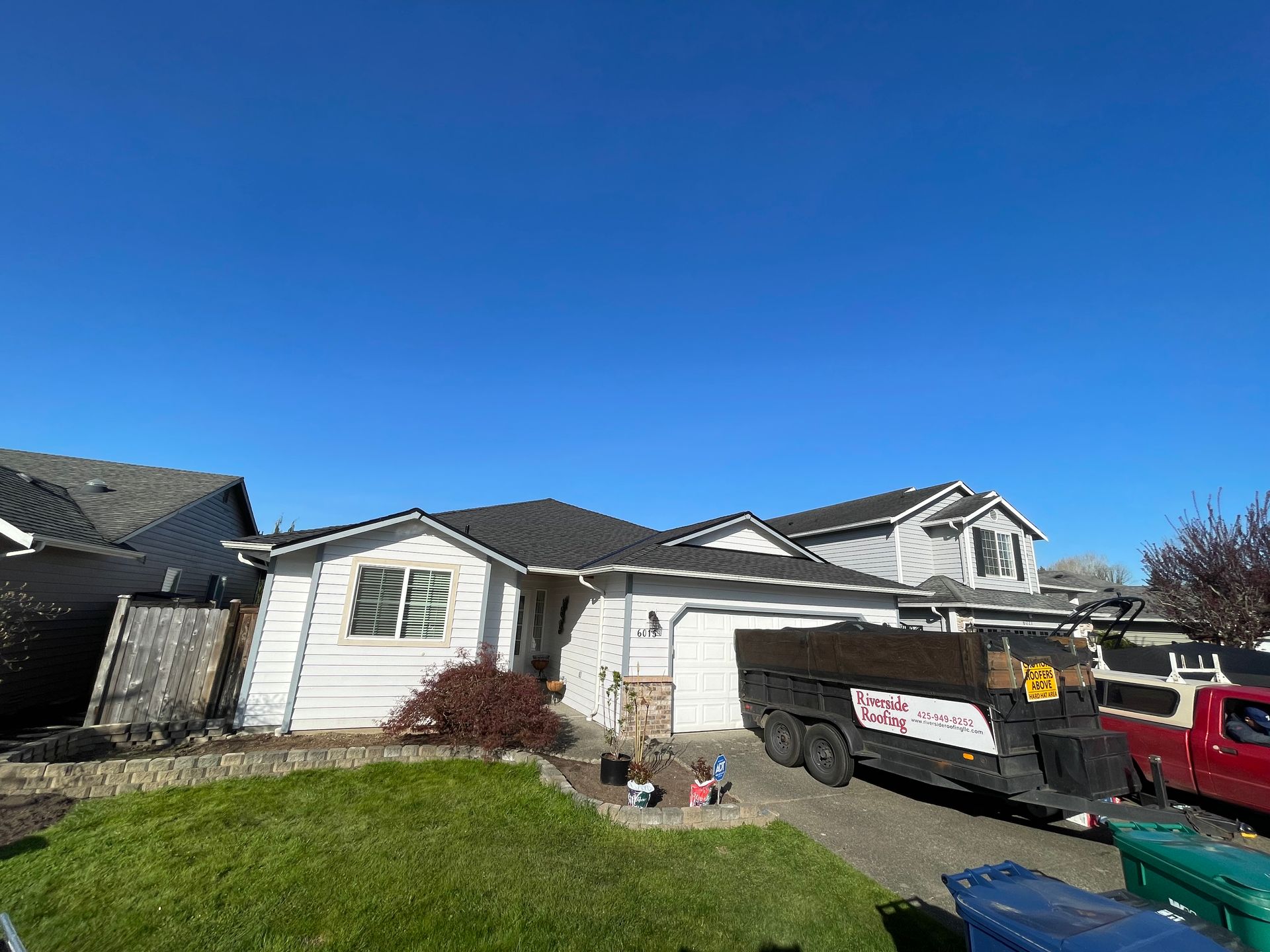 A dump truck is parked in front of a house on a sunny day taken by Riverside Roofing