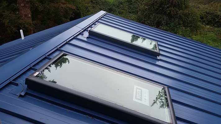 A blue roof with two skylights on it.