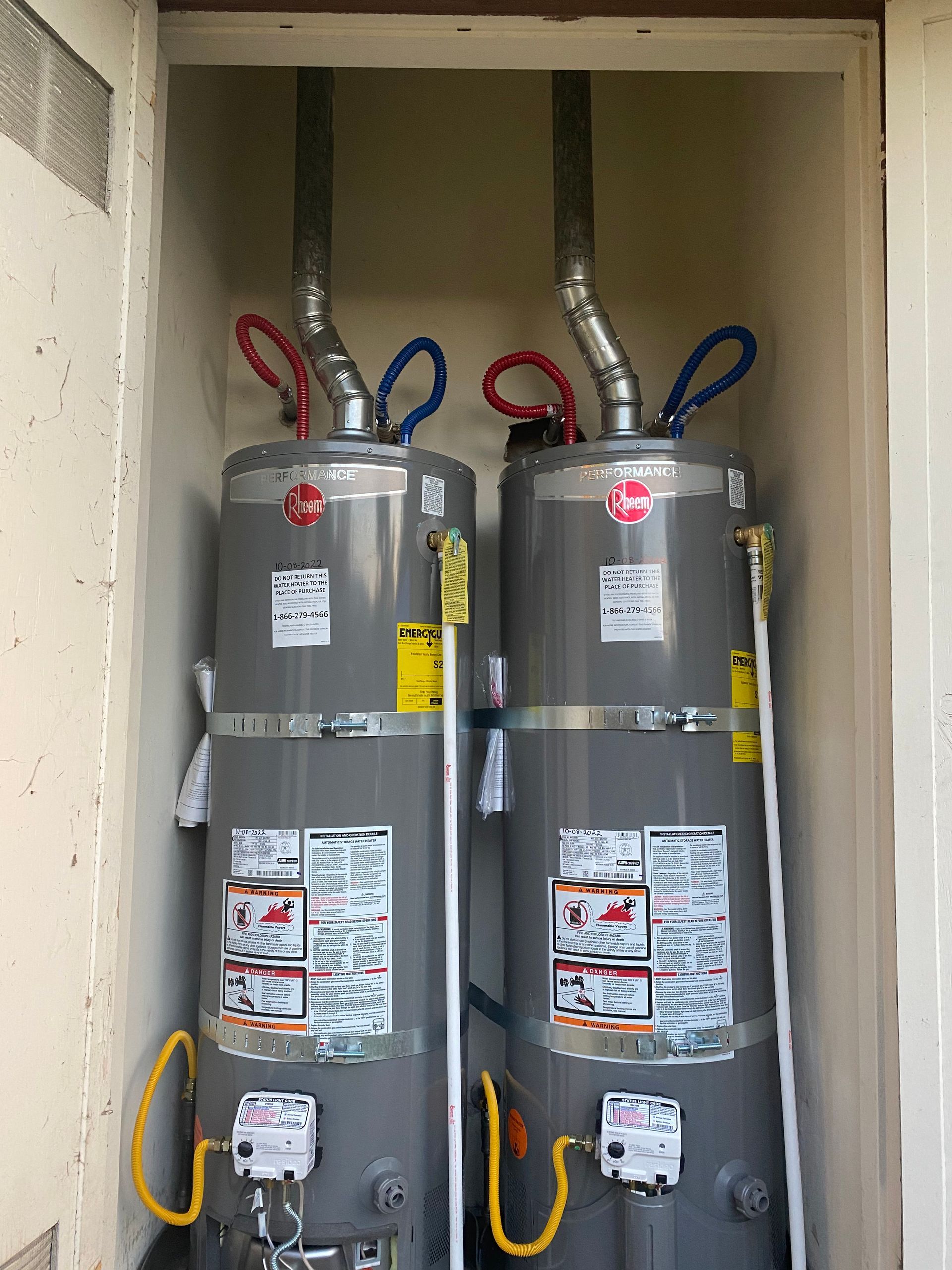 Two water heaters are sitting next to each other in a closet.