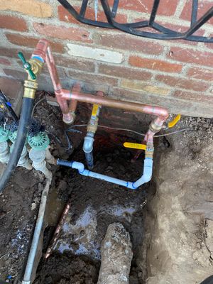 A hose is connected to a copper pipe in the ground next to a brick wall.