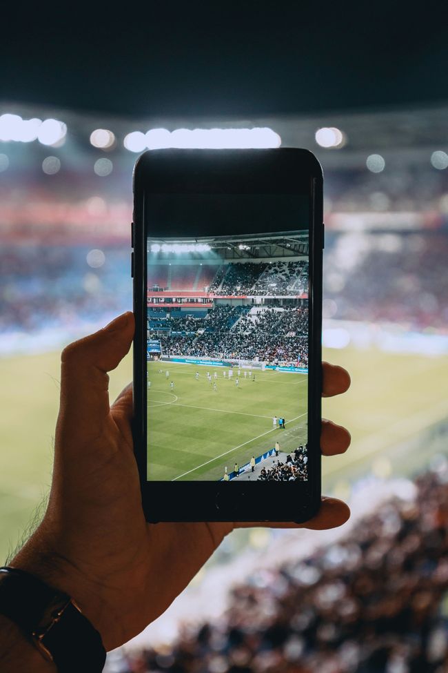 a person is holding a cell phone in their hand and taking a picture of a soccer field .