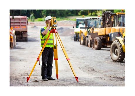 construction worker looking through surveying tripod on active construction site