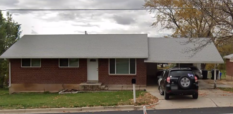 A brick house with a car parked under a carport on a cloudy day.