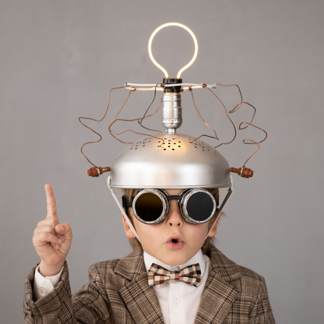 Child wearing a lightbulb headpiece and goggles, pointing up with a surprised expression.