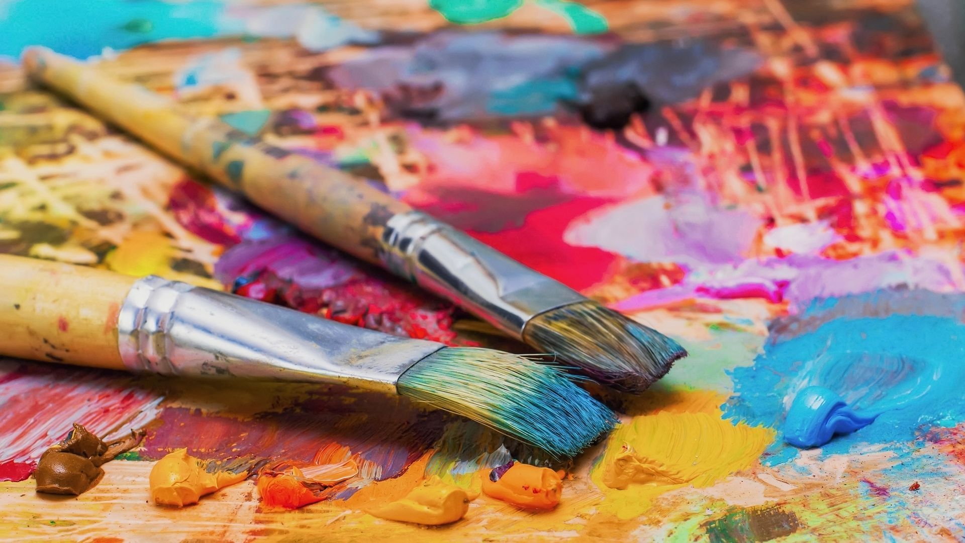 Paintbrushes on a colorful palette of mixed paints; close-up shot.