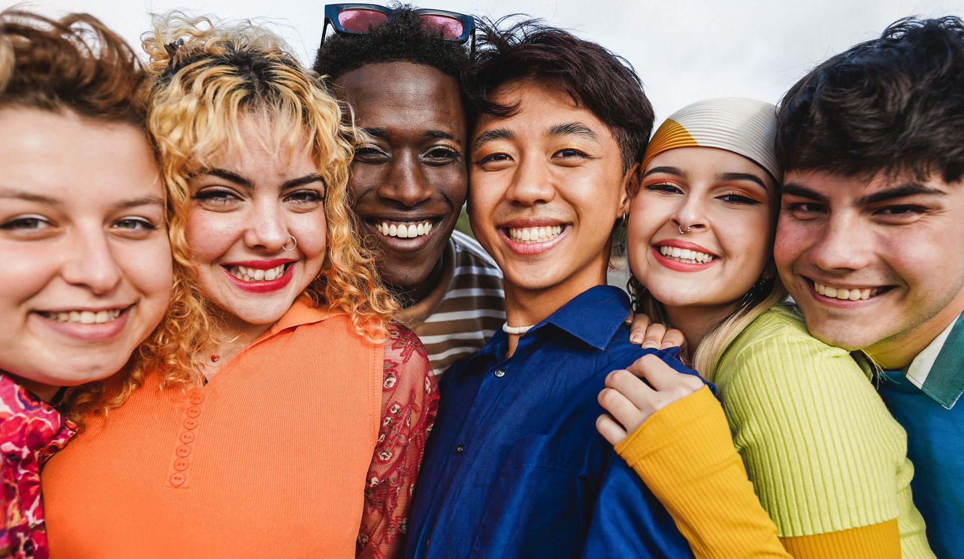 Group of six smiling people posing for a photo, diverse skin tones, outdoor setting.